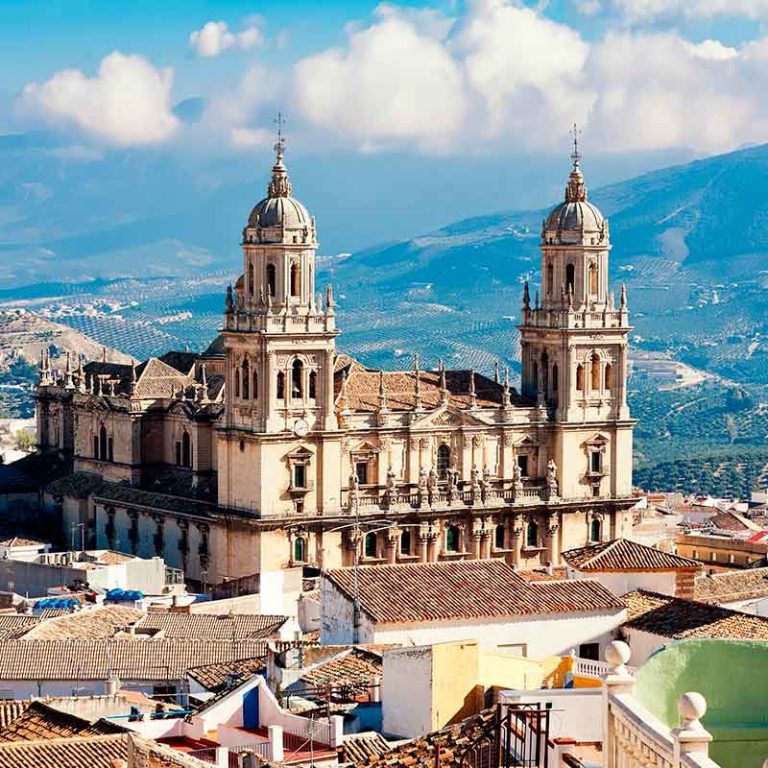 Vista panorámica de la catedral con torres en un paisaje montañoso y nubes.