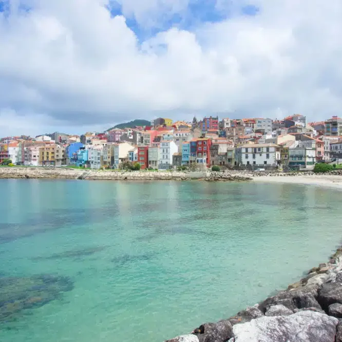 Vista de un colorido pueblo costero junto a aguas cristalinas y un cielo nublado.