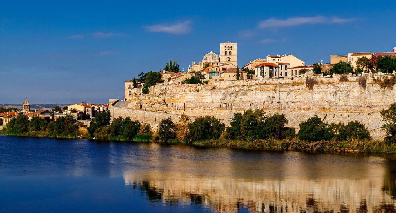 Vista de un río con un acantilado y un pueblo en la cima, bajo un cielo azul claro de ZAMORA.