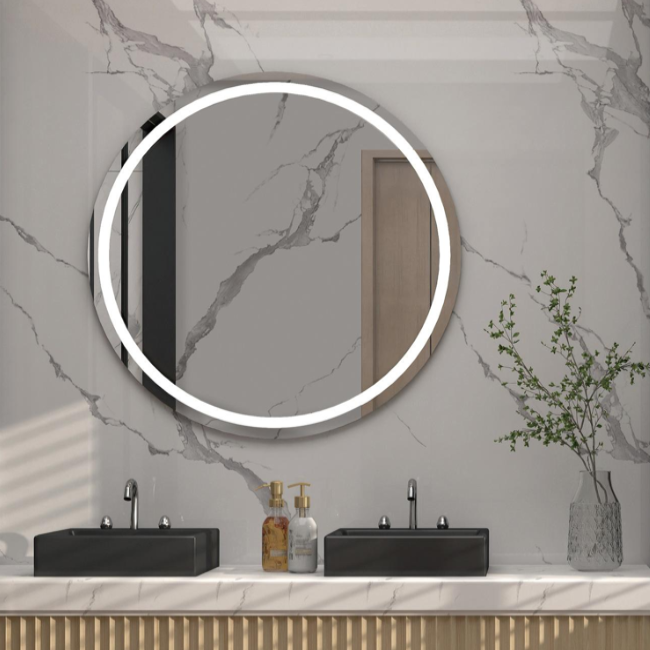 Baño con placas decorativas en la pared, espejo redondo iluminado sobre un lavabo de mármol con dos grifos y un ramo de flores.