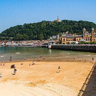 Playa con personas, edificios y montañas al fondo en un día soleado.
