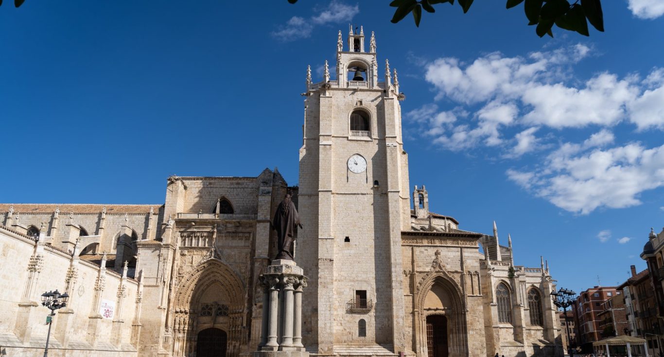 Fachada de una catedral con torre y reloj, cielo azul con nubes EN PALENCIA