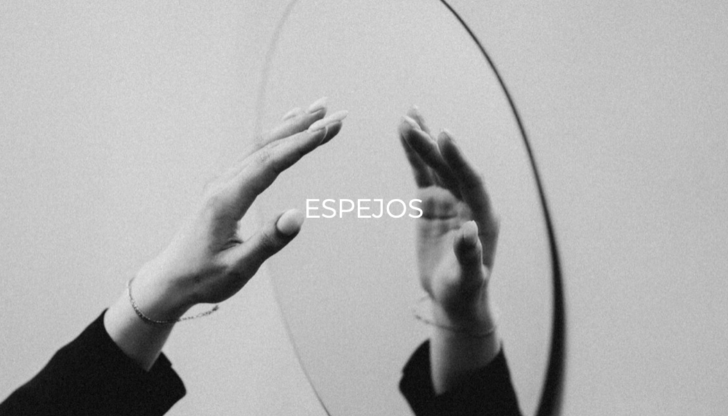 Una mano toca un espejo circular con el texto "ESPEJOS" en el centro.
