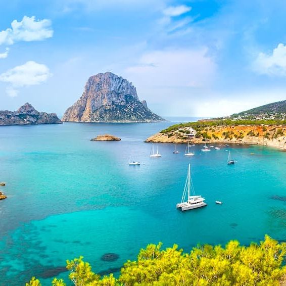 Vista serena de una costa mediterránea con un barco y montañas al fondo.