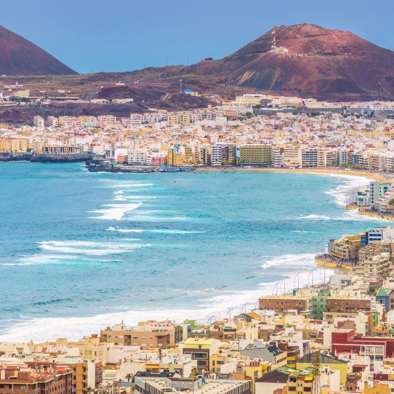 Vista de la costa con montañas, edificios y olas del mar.
