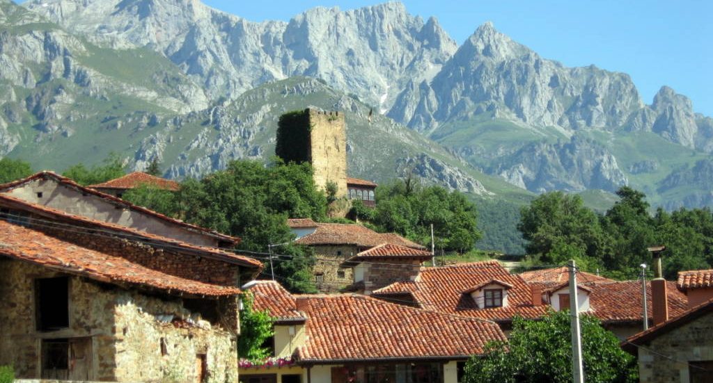 Vista de un pueblo con casas de tejado rojo y una torre, rodeado de montañas en Santander