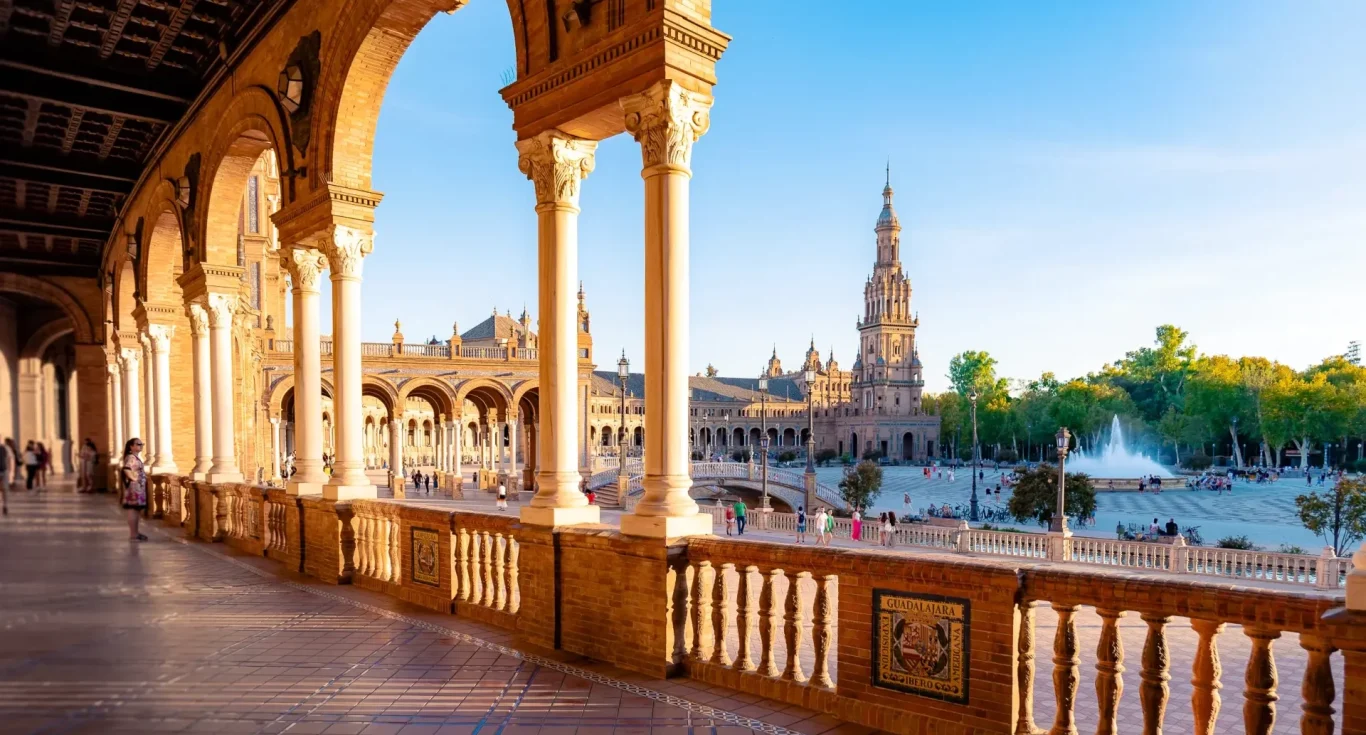 Vista desde un pórtico con columnas hacia una plaza con un monumento y árboles en SEVILLA ESPAÑA