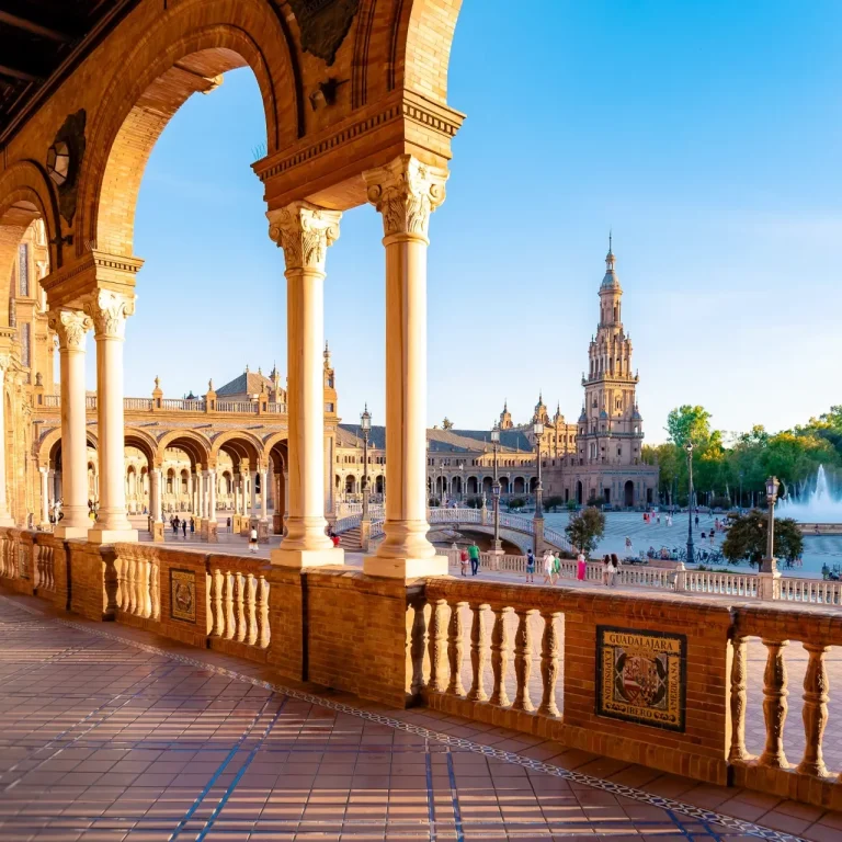 Vista del Plaza de España en Sevilla, con arcos, columnas y la torre al fondo.