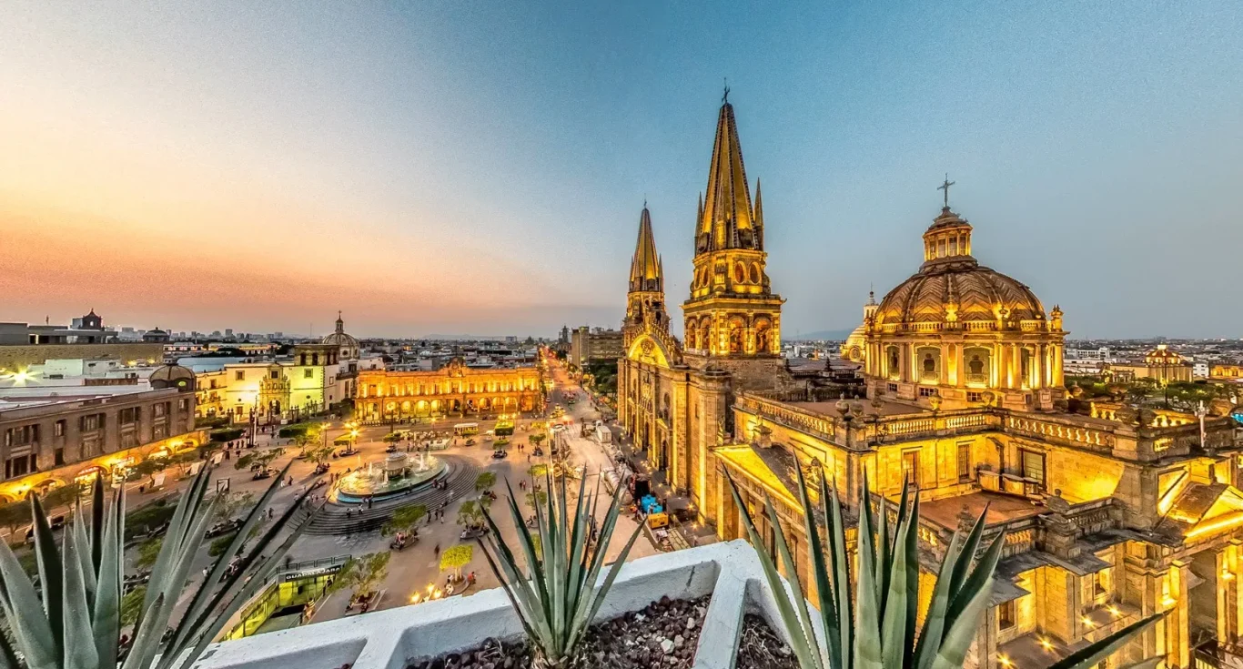 Vista panorámica de la ciudad de Guadalajara al atardecer, con catedrales y edificios históricos.