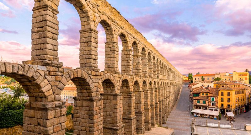 Acueducto romano de Segovia al atardecer, con cielo colorido y edificios cercanos.