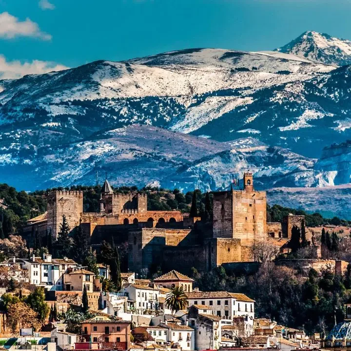 Castillo sobre una colina con montañas nevadas al fondo y casas en la base.