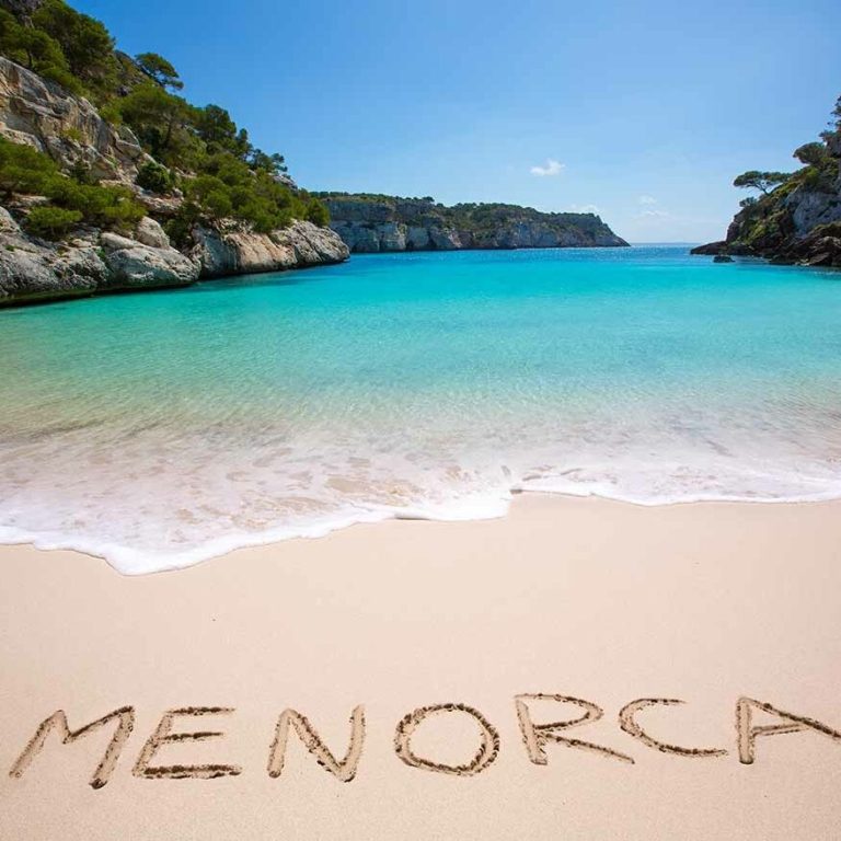Playa de Menorca con agua turquesa y palabras escritas en arena.