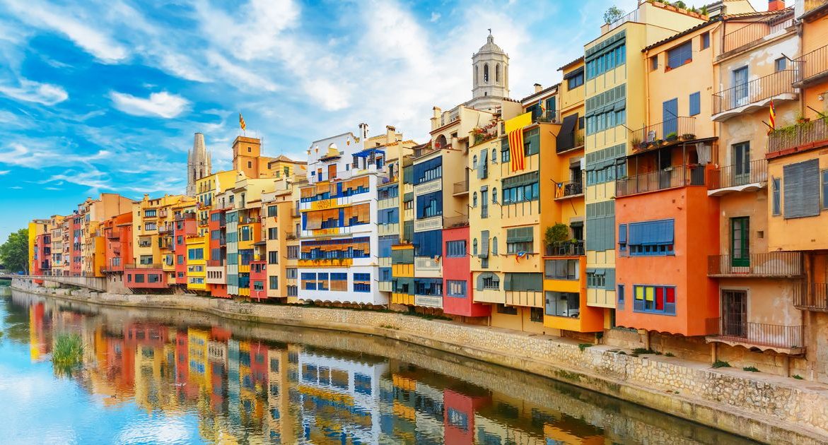 Ribera del río con casas coloridas reflejadas en el agua, bajo un cielo azul de Girona.