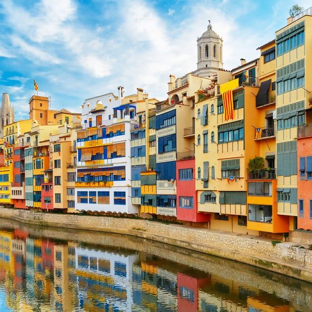 Casas coloreadas a la orilla de un río en Girona, bajo un cielo despejado.