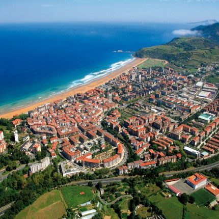 Vista aérea de una costa con playas, ciudad y montañas al fondo.
