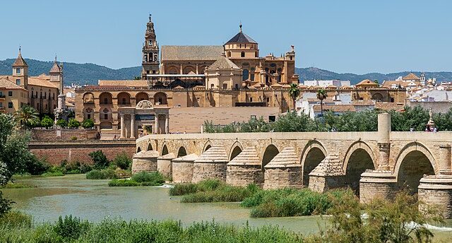 Puente sobre el río con la iglesia de la ciudad de fondo y un paisaje soleado en Córdoba
