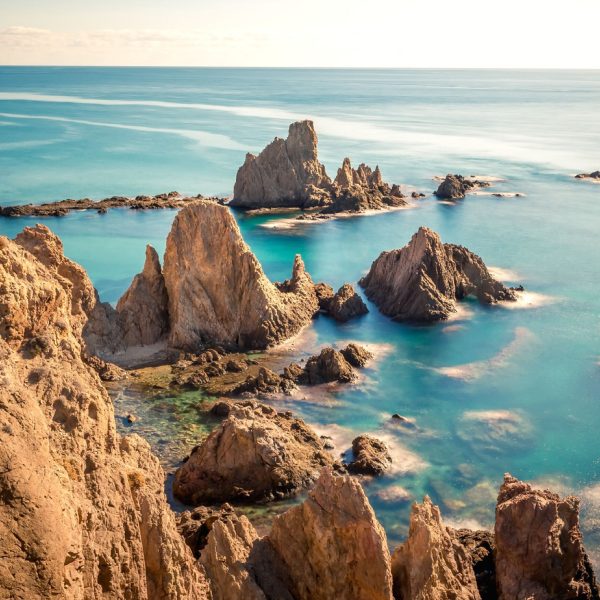 Vista de rocas en el mar con agua clara y cielo despejado al fondo de Almeria.