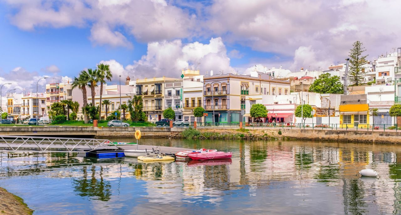 Paseo junto a un canal con barcos de colores y edificios coloridos al fondo EN huelva