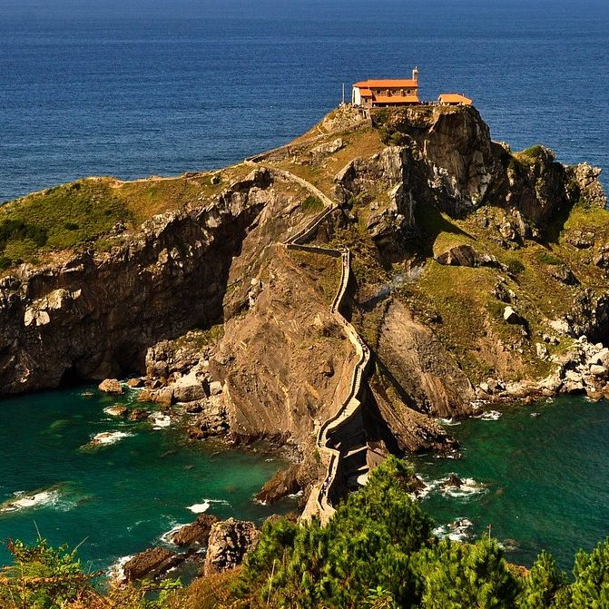Un camino de piedra lleva a una pequeña ermita sobre un acantilado junto al mar.