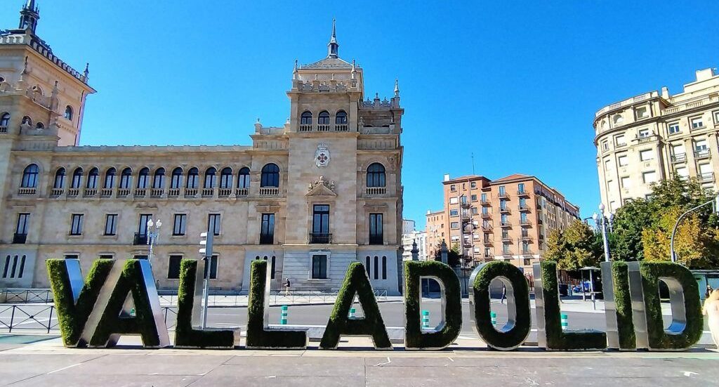 Texto grande "VALLADOLID" en un entorno urbano soleado frente a un edificio histórico.