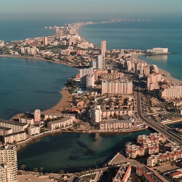 Vista aérea de una costa con edificios y una playa, rodeada de agua.