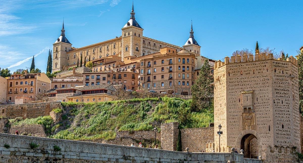Castillo y murallas de Toledo, rodeado de paisajes verdes y cielos despejados.