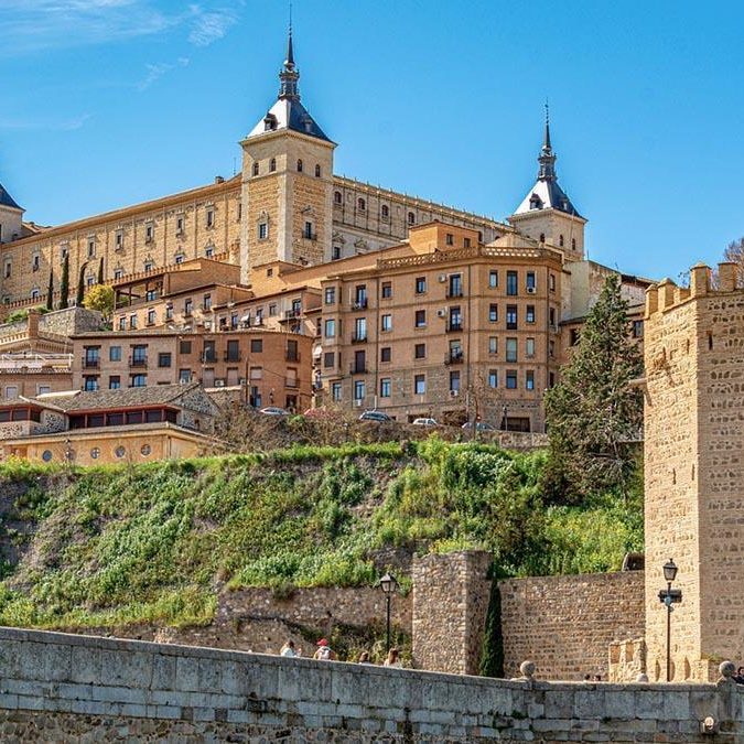 Castillo y fortificaciones en una colina, con edificios históricos y cielo azul de fondo.