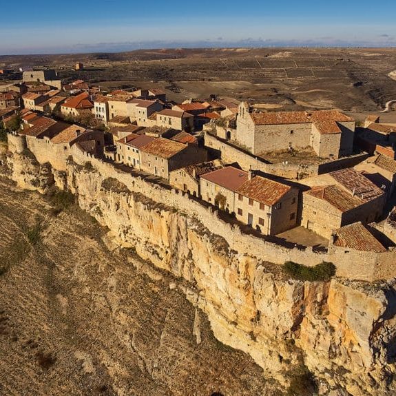 Pueblo histórico situado sobre un acantilado, con casas de piedra y tejados de teja.