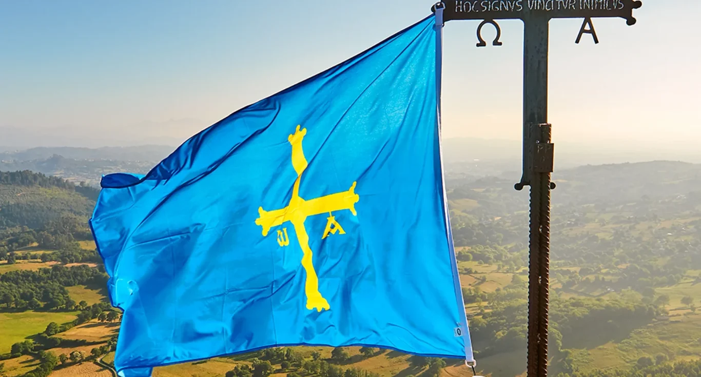 Bandera de Asturias ondeando con un fondo de paisaje montañoso.