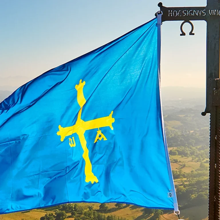 Bandera de Asturias con cruz amarilla sobre fondo azul, ondeando al viento.