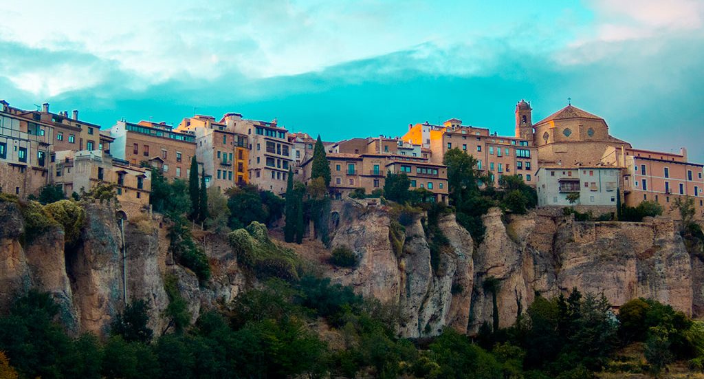 Vista panorámica de un pueblo histórico sobre acantilados con casas coloridas y vegetación en Cuenca.
