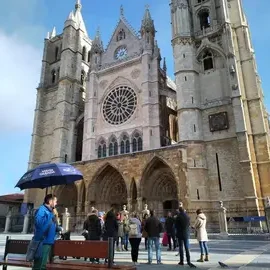 Catedral con torres altas y rosetón, personas bajo un paraguas en el primer plano.
